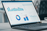 Laptop screen displaying colorful business analytics with bar charts, pie chart, and data tables on a white background.